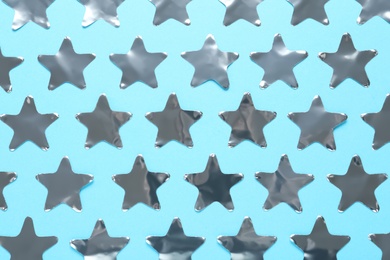 Shiny silver star shaped confetti on light blue background, flat lay