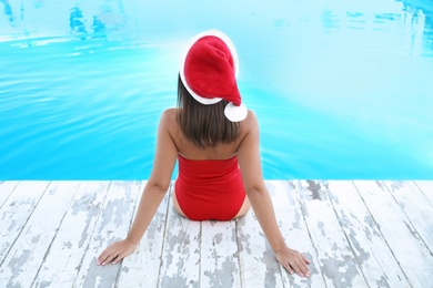 Young woman wearing Santa Claus hat near swimming pool, back view. Christmas vacation