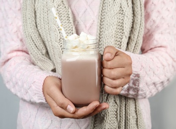 Woman holding mason jar of delicious cocoa drink with marshmallows, closeup