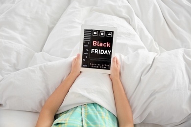 Woman using tablet with Black Friday announcement while lying in bed, above view
