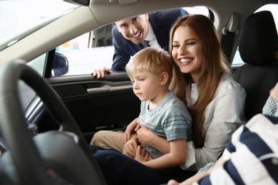 Young family choosing new car with salesman in salon