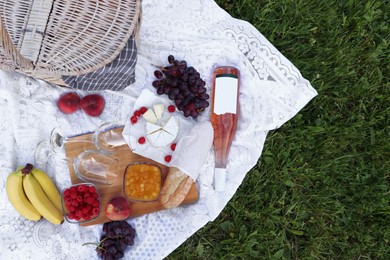 Picnic blanket with tasty food, basket and cider on green grass outdoors, flat lay