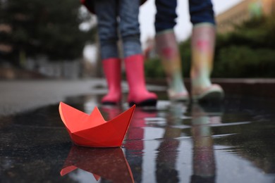 Little girl with her mother walking outdoors, focus on  paper boat in puddle