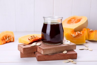 Photo of Fresh pumpkin seed oil in glass jar on white wooden table