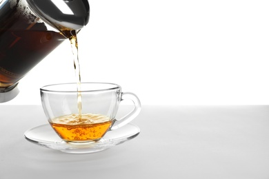 Pouring hot tea into glass cup on white background