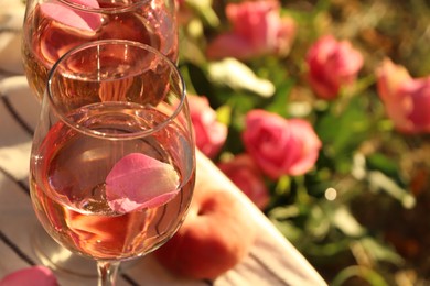 Photo of Glasses of delicious rose wine with petals outside, closeup. Space for text