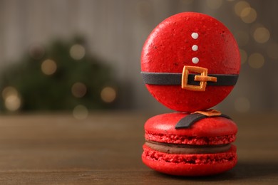 Photo of Beautifully decorated Christmas macarons on wooden table against blurred festive lights, space for text