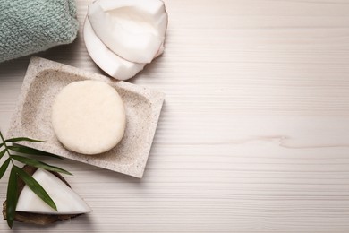 Photo of Solid shampoo bar, leaf and coconut on white wooden table, flat lay. Space for text