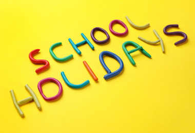 Photo of Phrase School Holidays made of modeling clay on yellow background