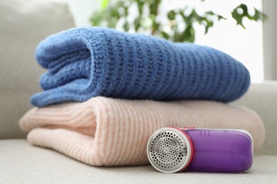 Photo of Modern fabric shaver and woolen sweaters on sofa indoors, closeup