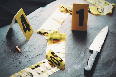 Evidence markers, yellow tape and knife on black slate table. Crime scene