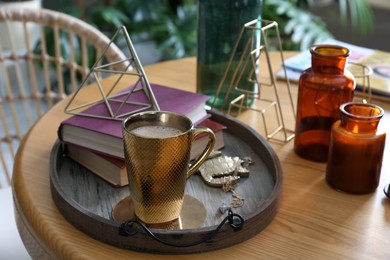 Wooden tray with decorations, books and hot drink on table indoors