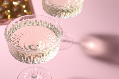 Photo of Glasses of expensive white wine on pink background, closeup. Space for text