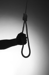 Silhouette of man holding rope noose on light background, closeup