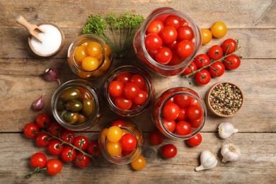 Pickling jars with fresh tomatoes on wooden table, flat lay