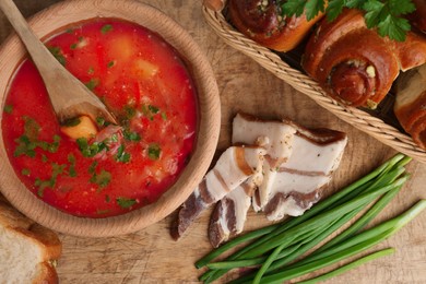 Photo of Delicious borsch served with pampushky and salo on wooden table, flat lay. Traditional Ukrainian cuisine