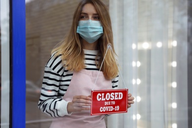 Business owner in mask hanging red sign with text Closed Due To Covid-19 onto glass door. Coronavirus quarantine