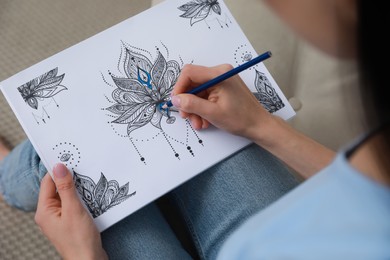 Young woman coloring antistress page on sofa, closeup