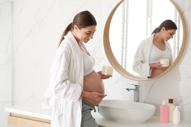 Young pregnant woman with cosmetic product in bathroom