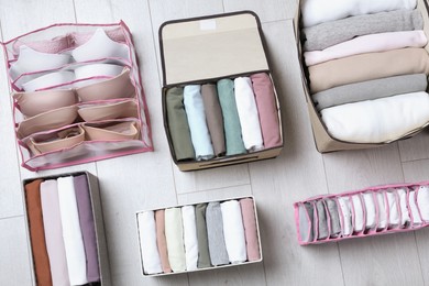Different organizers with folded clothes and underwear on white wooden background, flat lay. Vertical storage