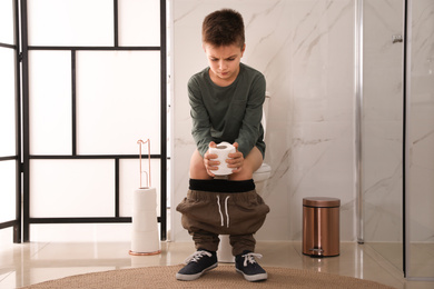Boy with paper suffering from hemorrhoid on toilet bowl in rest room