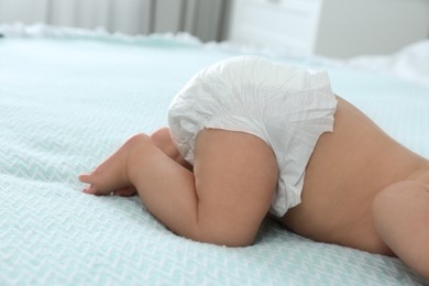 Photo of Cute little baby in diaper on bed at home, closeup