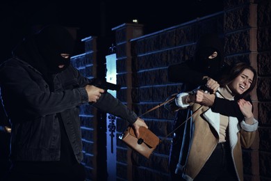 Photo of Thieves with weapons stealing woman's bag outdoors at night. Self defense concept