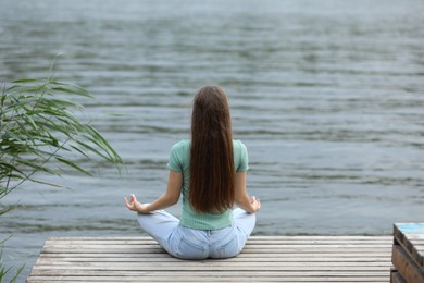 Photo of Teenage girl meditating near river, back view