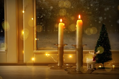 Burning candles and festive decor on window sill indoors. Christmas eve