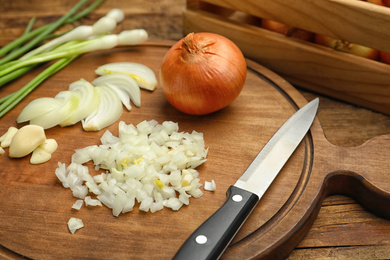 Board with cut onion and garlic on wooden table, closeup