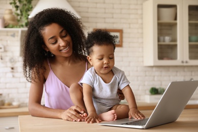 African-American woman and her baby with laptop in kitchen. Happiness of motherhood