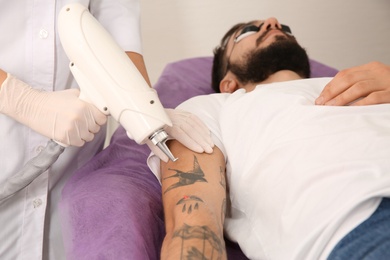 Young man undergoing laser tattoo removal procedure in salon