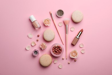 Flat lay composition with makeup products, roses and macarons on pink background