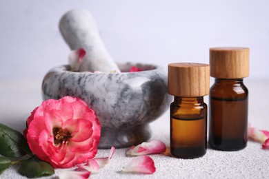 Glass bottles of aromatic essential oil, mortar with roses on white table, closeup