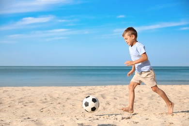 Cute little boy playing with football ball on sandy beach