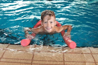 Little boy with swimming noodle in indoor pool