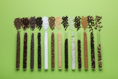 Test tubes with various spices on green background, flat lay