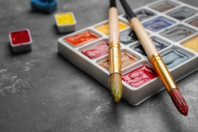 Plastic palette with colorful paints and brushes on grey table