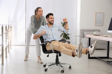 Office employee giving her colleague ride in chair at workplace