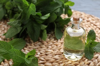 Bottle of essential oil and mint on wicker mat, closeup