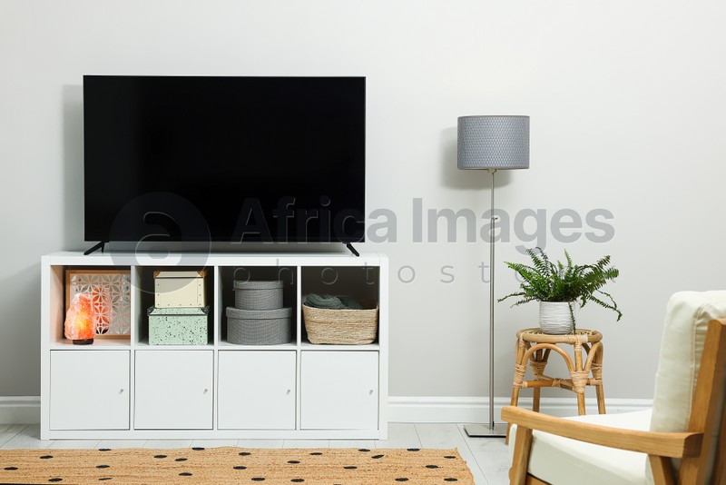 Photo of Modern TV on cabinet, armchair and beautiful houseplant indoors. Interior design