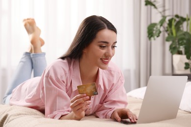 Woman with credit card using laptop for online shopping in bedroom