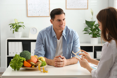 Young nutritionist consulting patient at table in clinic