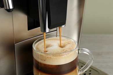 Modern coffee machine making latte into glass cup on wooden table, closeup
