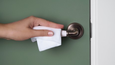 Photo of Woman cleaning doorknob with wet wipe indoors, closeup. Protective measures