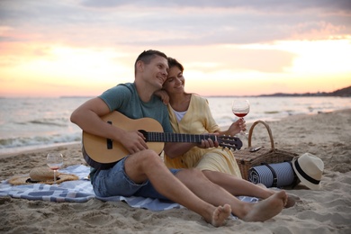 Lovely couple with guitar and picnic basket on beach at sunset