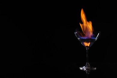 Cocktail glass with flaming vodka on black background, space for text