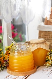 Delicious fresh honey and beautiful flowers on white wooden table indoors