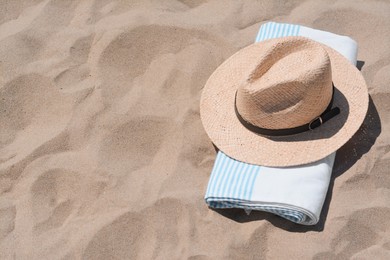 Straw hat and beach towel on sand, space for text