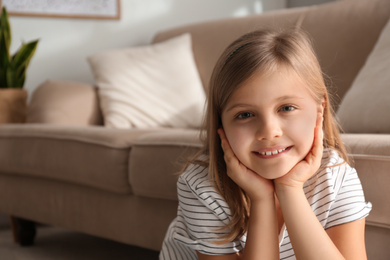 Cute little girl near couch at home. Space for text